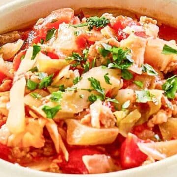 A bowl of cabbage soup with ground meat, tomatoes, and fresh herbs, garnished with chopped parsley.