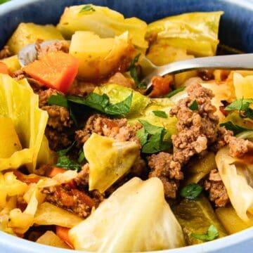 A bowl of cabbage stew with ground beef, potatoes, carrots, and herbs—one of our favorite budget recipes—served with a spoon.