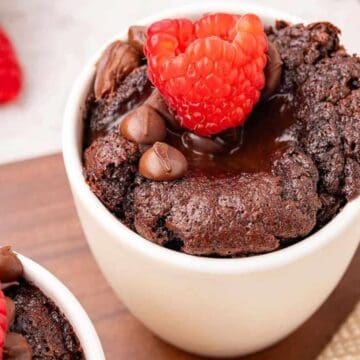 Chocolate mug cake topped with fresh raspberries and chocolate chips, served in a white cup.