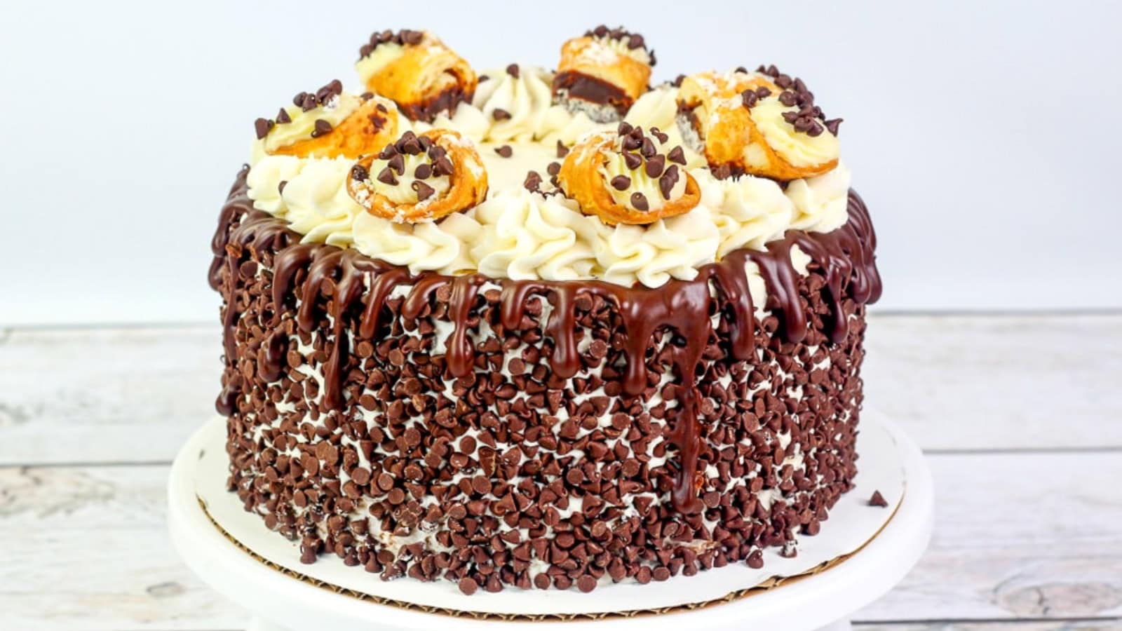 A chocolate chip cake with chocolate ganache, cream swirls, and cream puffs on top.