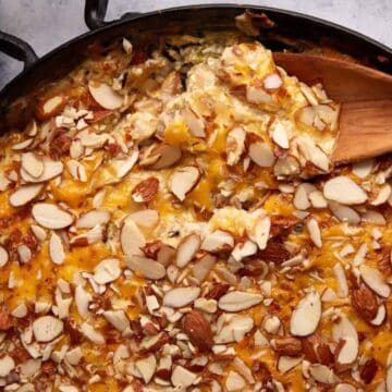 A casserole topped with sliced almonds and melted cheese, with a wooden spoon scooping a portion.