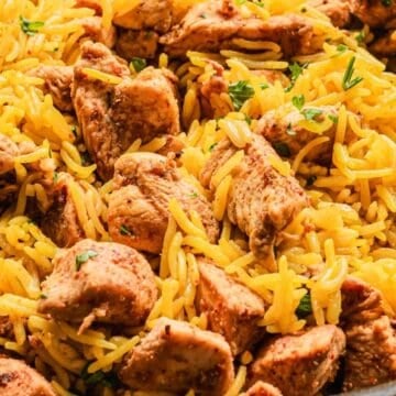 Close-up of yellow rice and seasoned chicken pieces garnished with herbs in a pan-perfect for easy dinners.