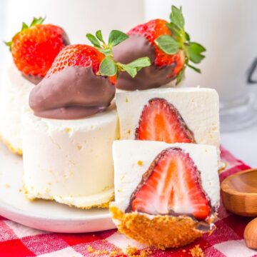 Mini cheesecakes topped and filled with chocolate-covered strawberries on a white plate and red checkered cloth.