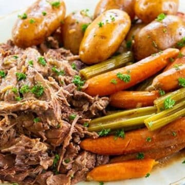 A plate of pot roast features shredded beef, baby potatoes, carrots, celery, and fresh parsley on top—one of those classic recipes that brings comfort to the table.