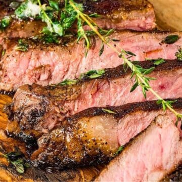 Sliced medium-rare steak on a wooden board, garnished with fresh herbs.