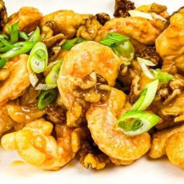 Honey walnut shrimp topped with sliced green onions on a white plate.