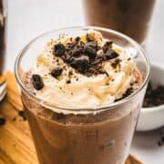 A glass of chocolate mousse topped with whipped cream and chocolate shavings on a wooden board.