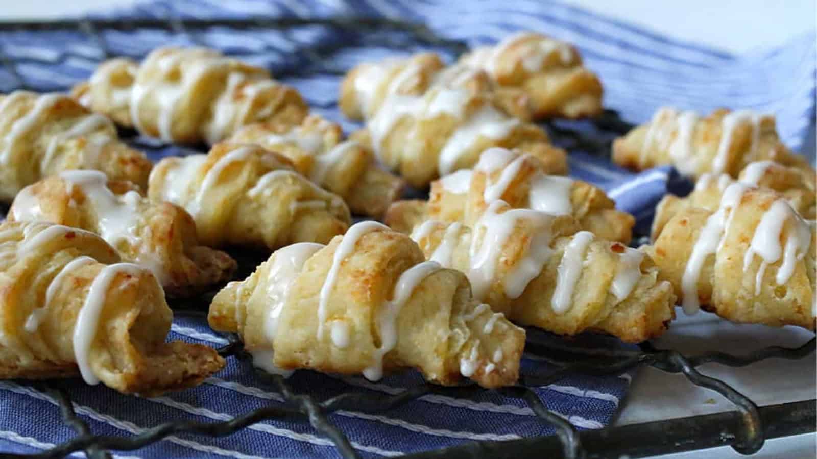 Iced crescrent rolls on a cooling rack with a bowl of icing.