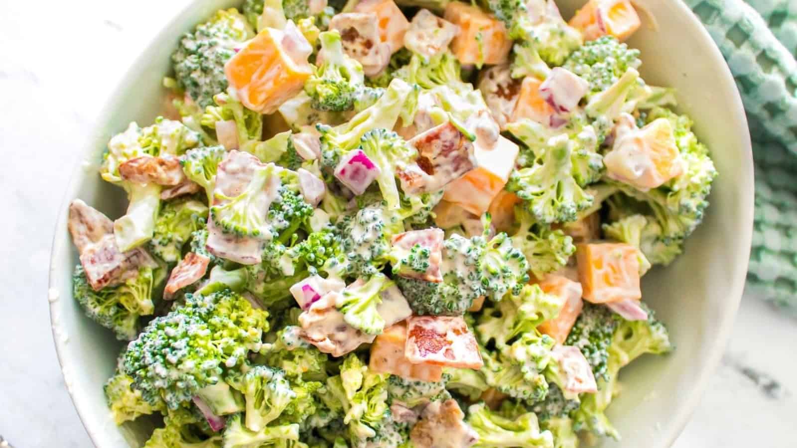 Close-up of a broccoli salad with diced cheddar cheese, red onions, bacon, and creamy dressing.