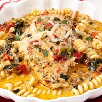 Perfect for cozy dinners, this creamy chicken breast with rotini pasta, tomatoes, and herbs is served in a white dish on a vibrant red plate.