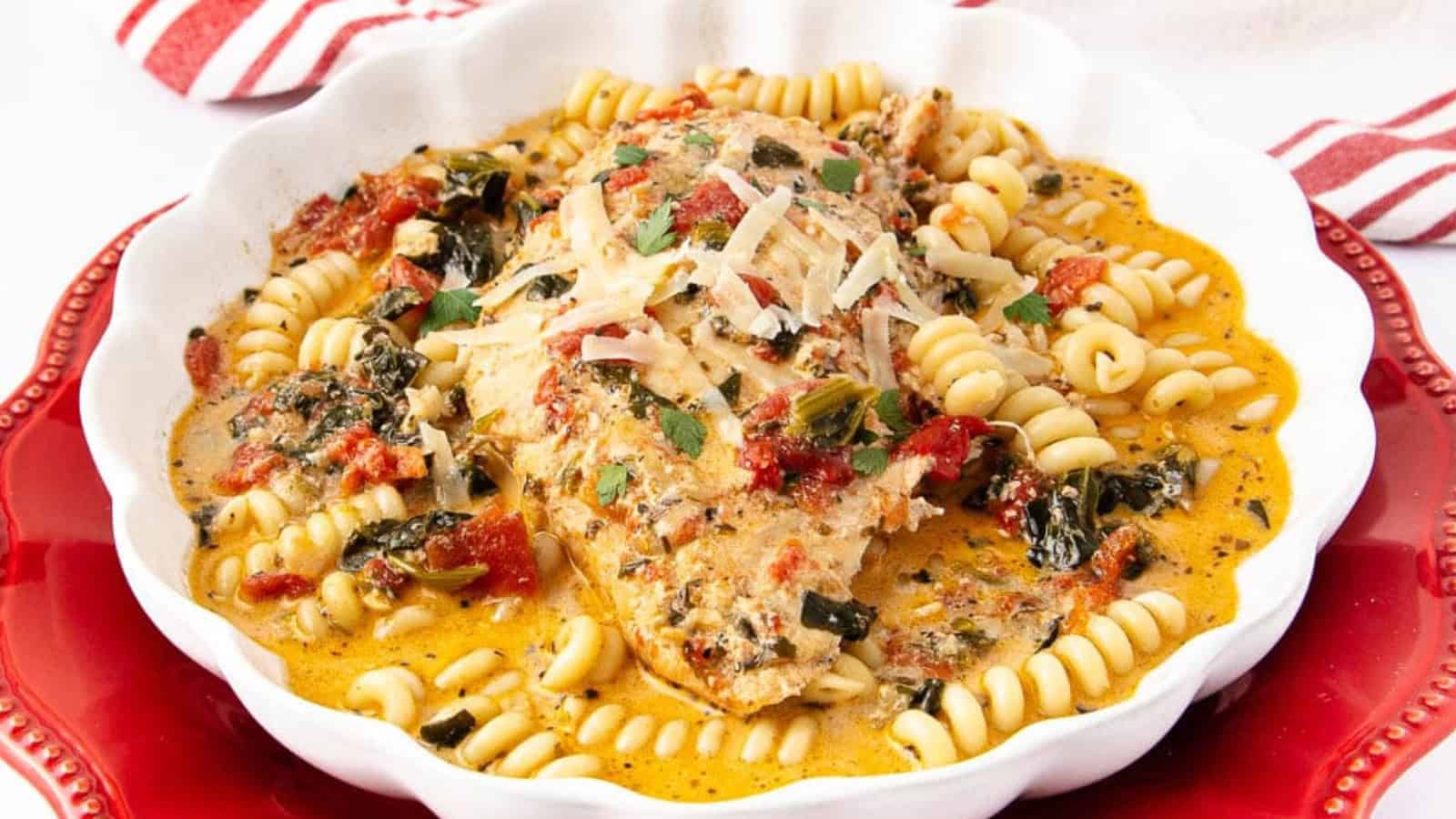 Perfect for cozy dinners, this creamy chicken breast with rotini pasta, tomatoes, and herbs is served in a white dish on a vibrant red plate.