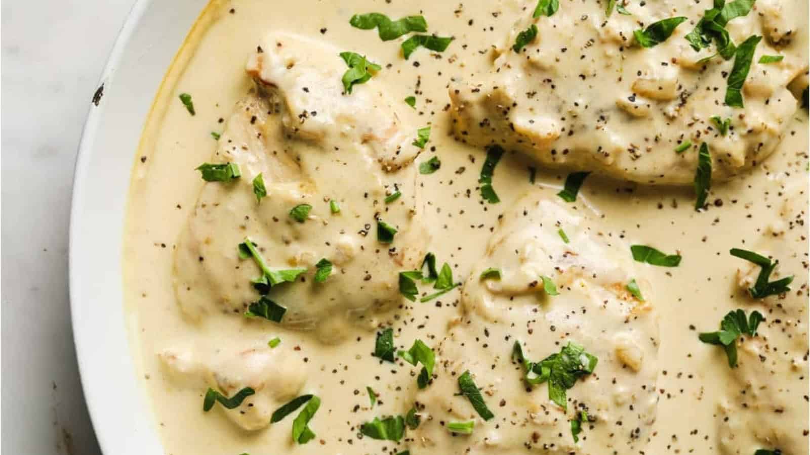 A white skillet of creamy garlic chicken garnished with herbs.