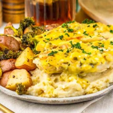 A plate of mashed potatoes, baked chicken with sauce, and roasted potatoes with broccoli, garnished with herbs.