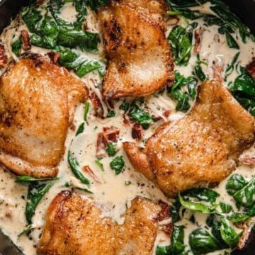Golden chicken thighs in creamy sauce with spinach and sun-dried tomatoes in a skillet.