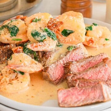 Sliced steak topped with creamy shrimp and spinach sauce on a white plate.