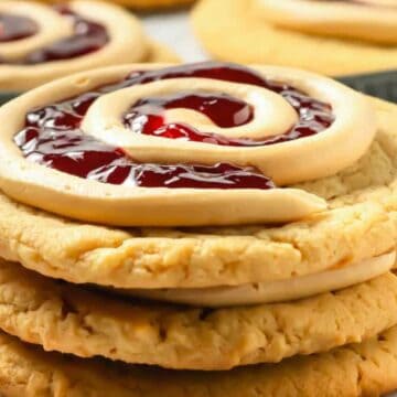 A stack of cookies topped with a swirl of icing and red jelly filling, with more cookies in the background.