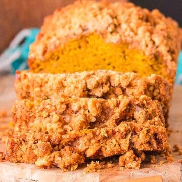 Sliced loaf of crumb-topped pumpkin bread on a wooden cutting board.