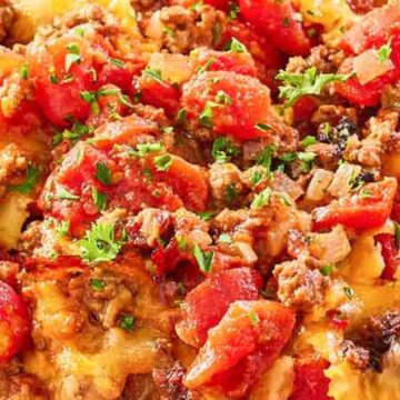 A plate of cheesy ground beef casserole, inspired by vintage recipes, topped with chopped tomatoes and fresh herbs.
