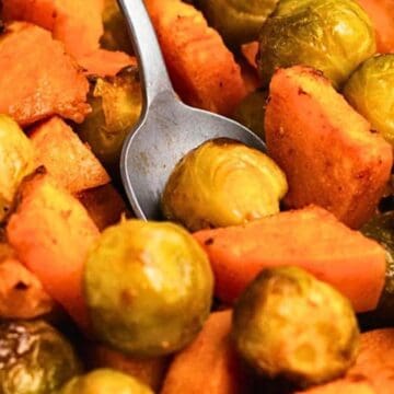 Roasted Brussels sprouts and sweet potato chunks with a silver fork nestled among the vegetables.