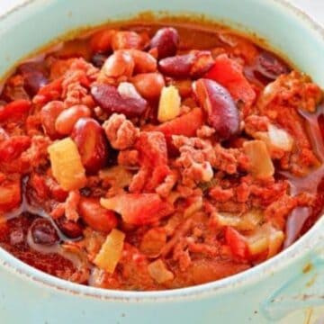 A bowl of chili with ground meat, beans, tomatoes, and diced vegetables, surrounded by tortilla chips.