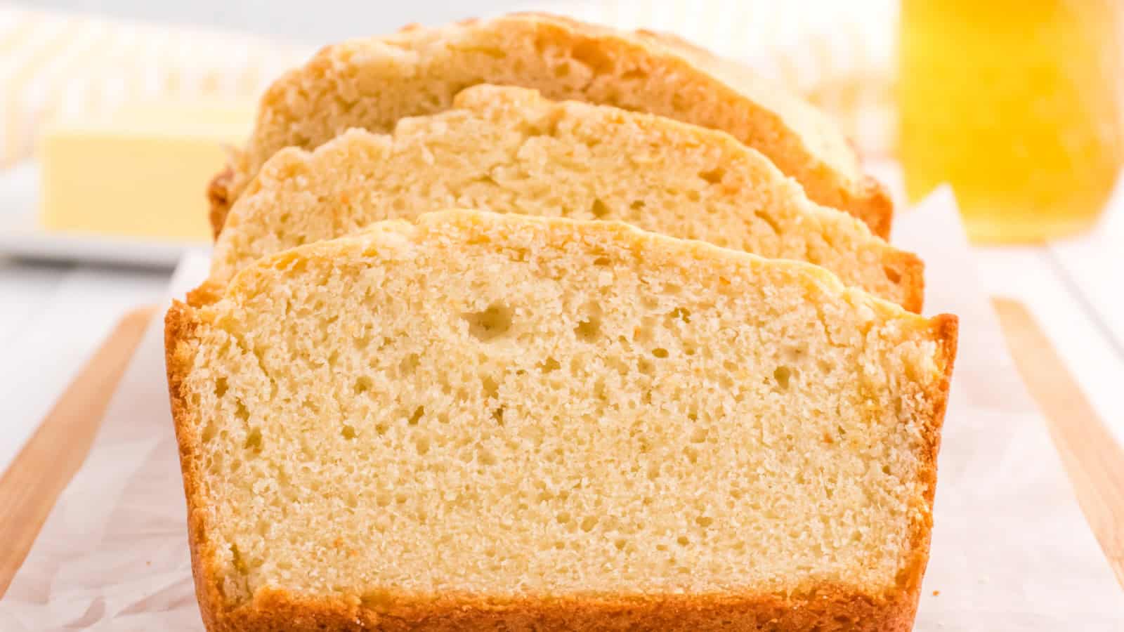 Sliced loaf of homemade bread on parchment paper, with a blurred background of butter and honey.