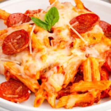 Baked penne pasta with melted cheese, pepperoni slices, and fresh basil on a white plate.