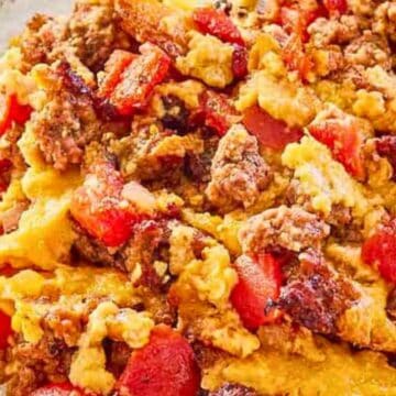 Scrambled eggs mixed with ground sausage and diced tomatoes on a plate, with a fork on the side.