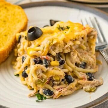 A plate of cheesy chicken and black bean casserole with a slice of garlic bread and a fork on the side.