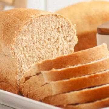 A loaf of whole wheat bread with several slices cut, placed on a white tray.