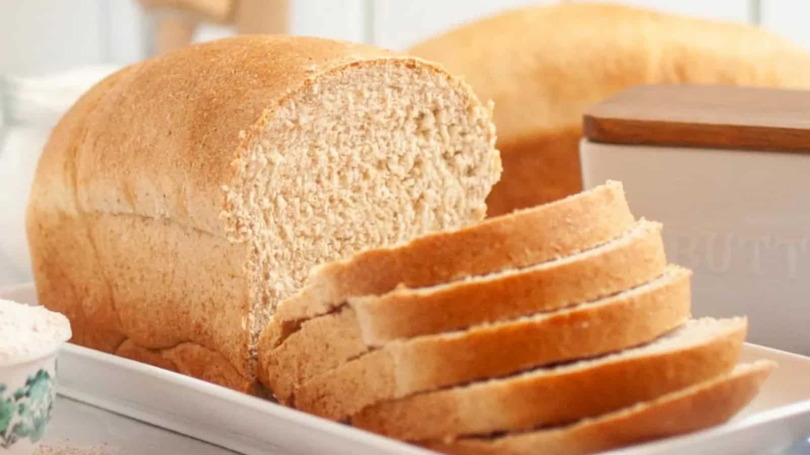 A loaf of whole wheat bread with several slices cut, placed on a white tray.