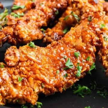 Close-up of crispy fried chicken tenders, made using Air Fryer Recipes, garnished with chopped parsley on a black plate.