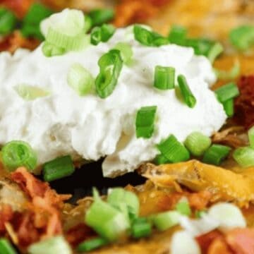 Close-up of loaded nachos topped with sour cream and chopped green onions.