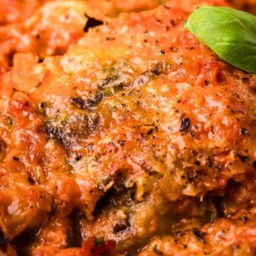 Close-up of cheesy baked lasagna with tomato sauce and herbs, garnished with fresh basil leaves.