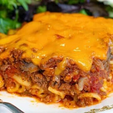 A slice of cheesy baked lasagna with ground meat and sauce, served with a side of mixed greens on a plate.