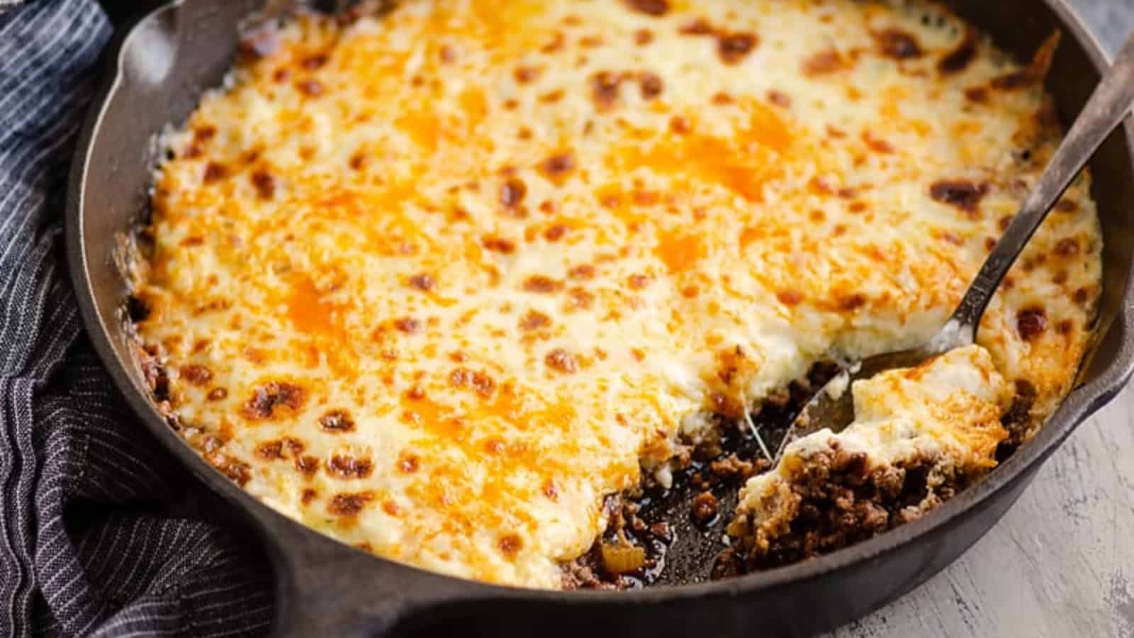 A cheesy baked casserole in a skillet, perfect for pantry-staple recipes, with a serving spoon and a portion removed.