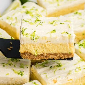 A spatula lifts a creamy lime bar with graham cracker crust, topped with whipped cream and lime zest.