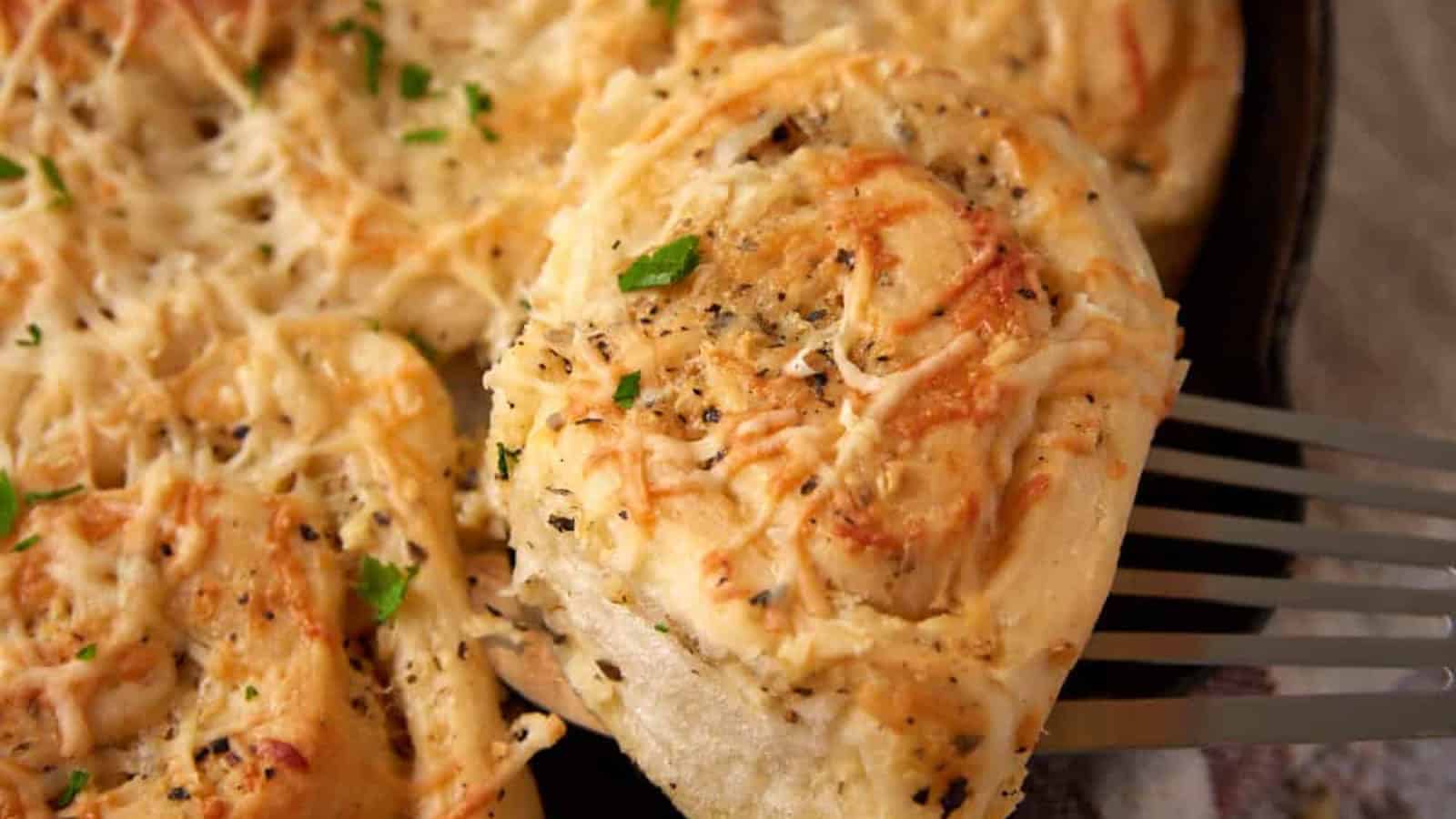 Cheesy garlic bread roll topped with herbs and cheese being lifted from a pan with a spatula.