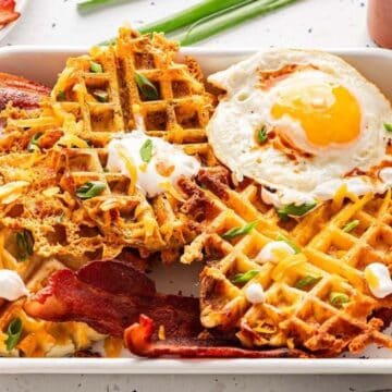 A plate of savory waffles topped with a sunny-side-up egg, bacon, sour cream, and chopped green onions.
