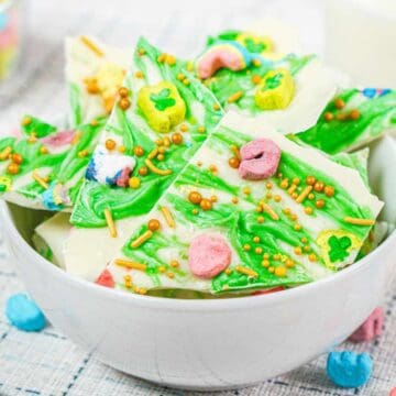 White chocolate bark with green swirls and colorful cereal pieces in a white bowl, with cereal scattered around.