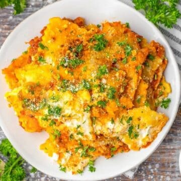 A plate of baked lasagna topped with herbs and cheese, with parsley and grated cheese on the side.