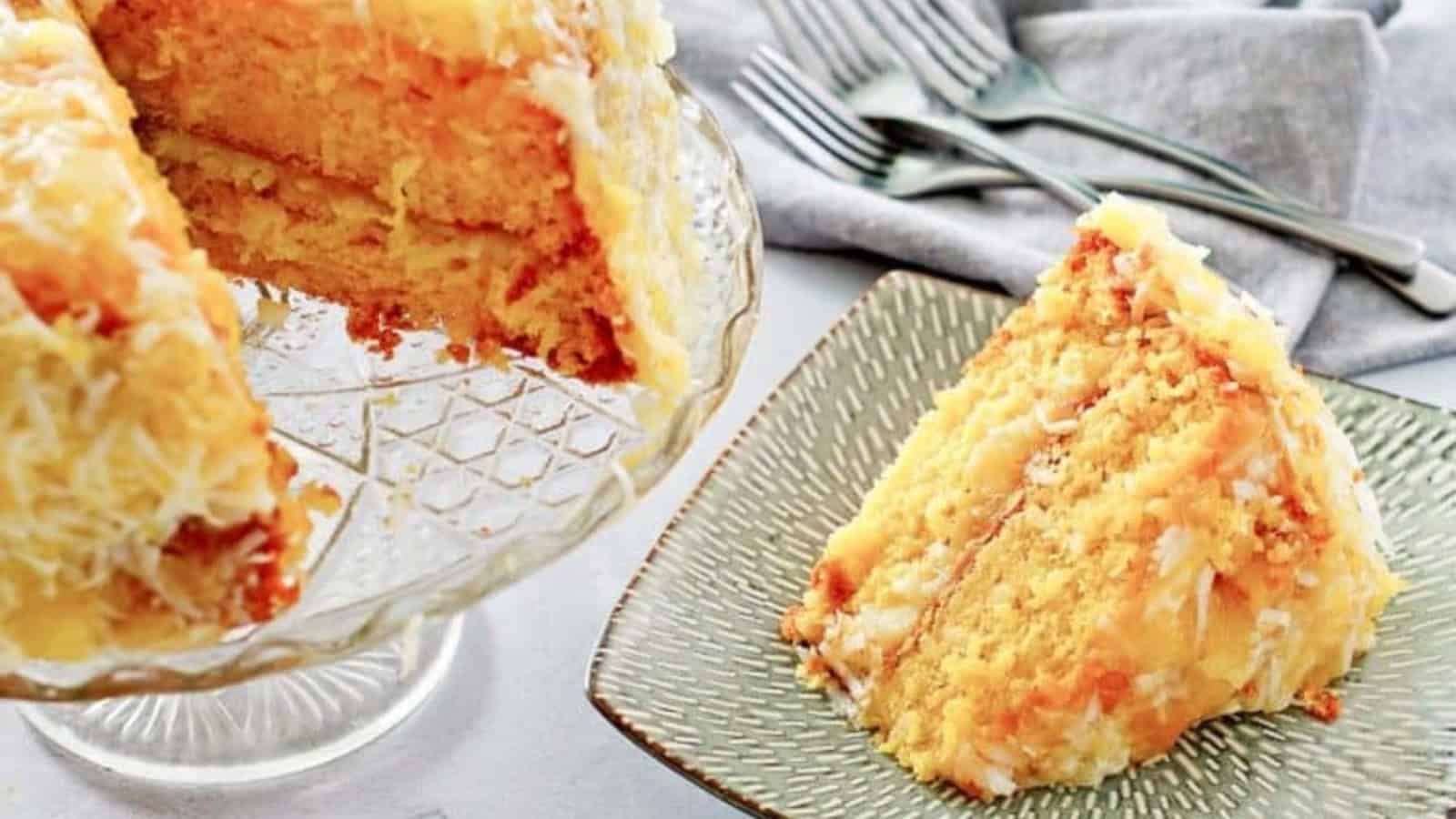 A slice of layered coconut cake on a plate, with the rest of the cake on a glass stand nearby.