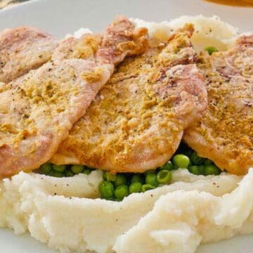 Three pieces of breaded pork on mashed potatoes with green peas on a white plate.