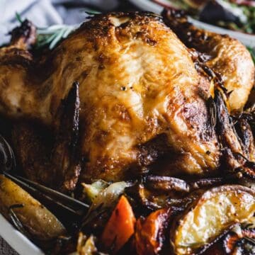 Roast chicken on a platter with vegetables and fresh rosemary, served with glasses of white wine.