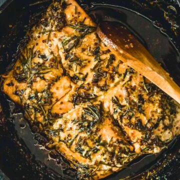 Baked salmon fillet with herbs in a cast iron skillet, stirred with a wooden spoon.