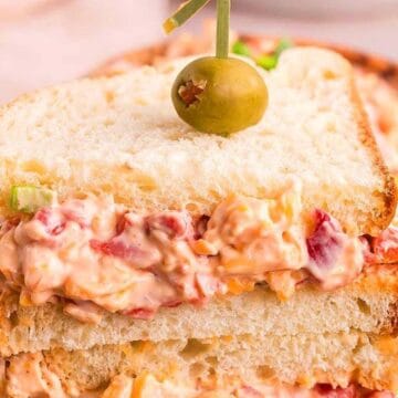 A stacked pimento cheese sandwich on white bread, garnished with a green olive on top.