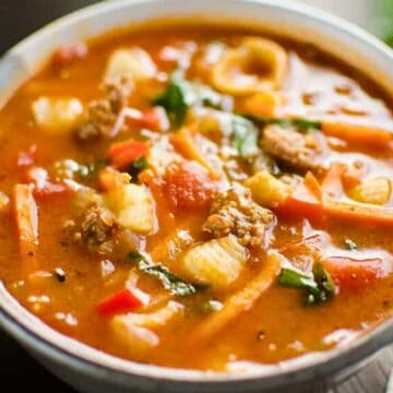 A bowl of hearty soup with pasta, ground meat, vegetables, and herbs, served with slices of bread.