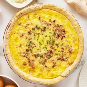 Quiche topped with chives on a table, surrounded by eggs, spices, and kitchenware.