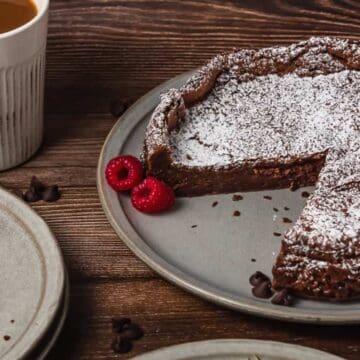A chocolate cake dusted with powdered sugar, with raspberries and a cup of coffee on a wooden table.