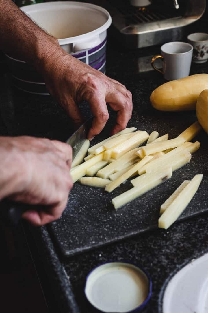 Hands slicing potatoes into thin strips on a cutting board, preparing them for delicious Russian Fried Potatoes in a cozy kitchen setting.