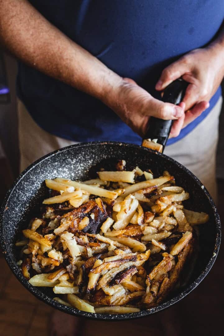 Person holding a frying pan filled with cooked, crispy Russian Fried Potatoes or hash browns.